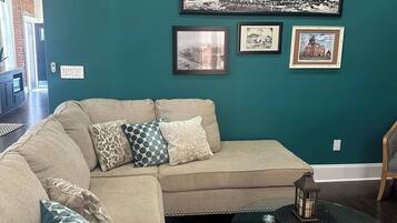 Ein Wohnzimmer mit einer türkisfarbenen Wand, einem Ecksofa und einem Couchtisch mit Glasplatte.