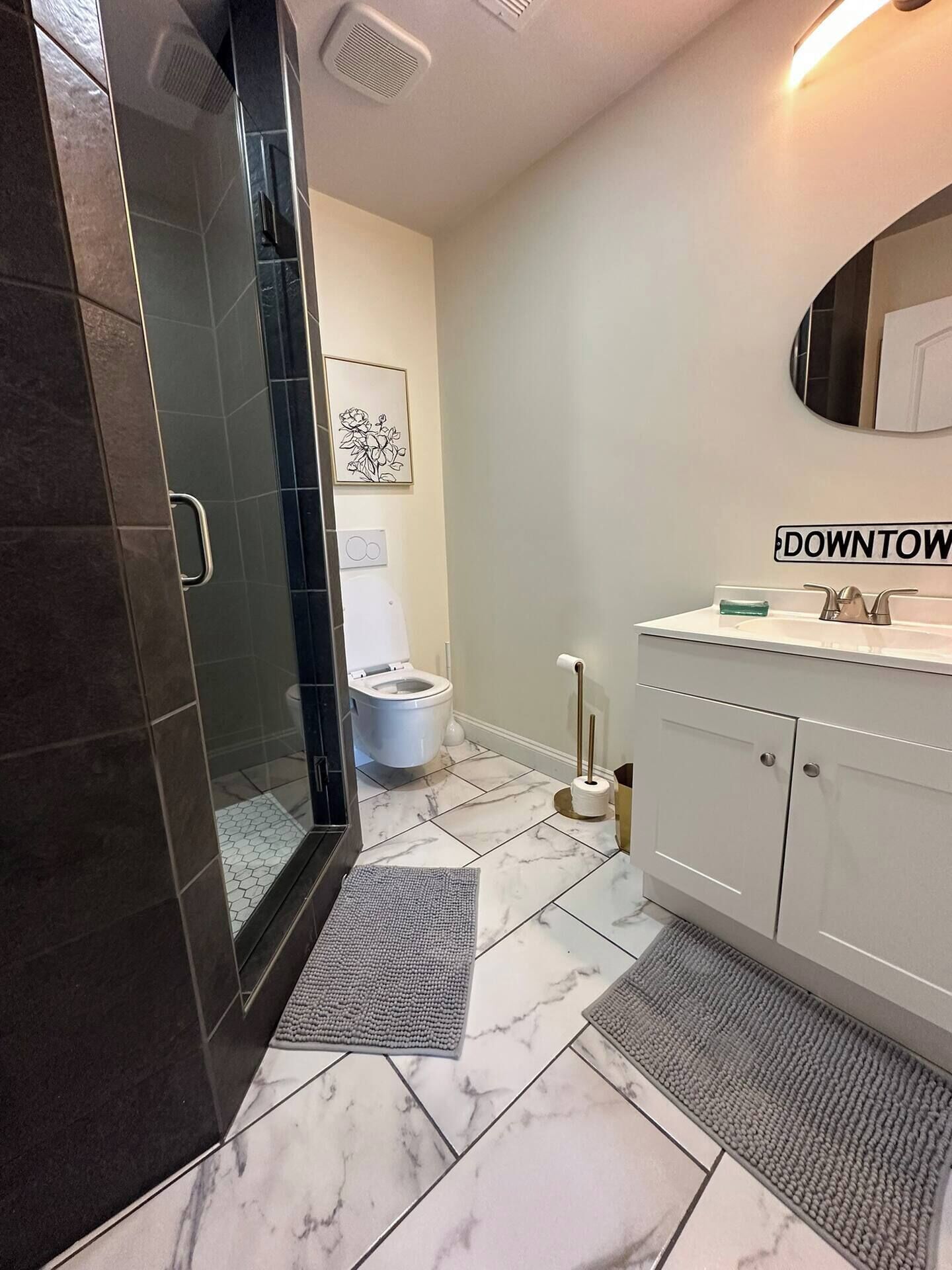 A bathroom with a glass shower enclosure, a toilet, a sink with a mirror, and a towel rack.
