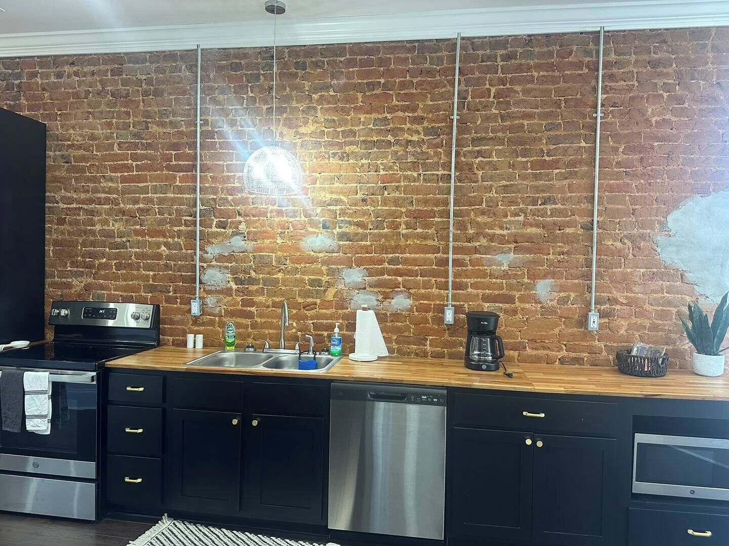 Una cocina con pared de ladrillo, electrodomésticos de acero inoxidable, encimera de madera y una lámpara colgante.