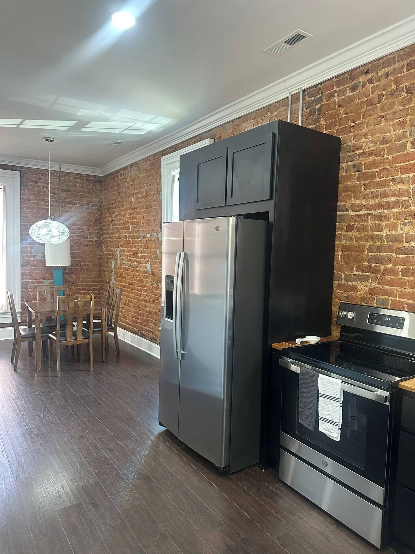 A kitchen with a stainless steel refrigerator, a black oven, and a dining area with wooden chairs and a table.