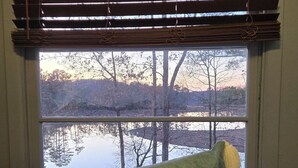 Una finestra con vista su un lago e alberi, un cuscino con la scritta 'Relax' e un letto con coperta verde.
