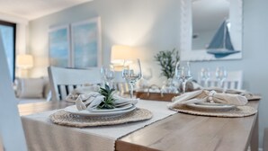 Uma área de refeições com uma mesa de madeira posta para uma refeição, com pratos brancos, guardanapos e copos.