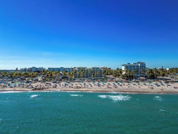 A beach resort with multiple hotel buildings, sun loungers, and palm trees.