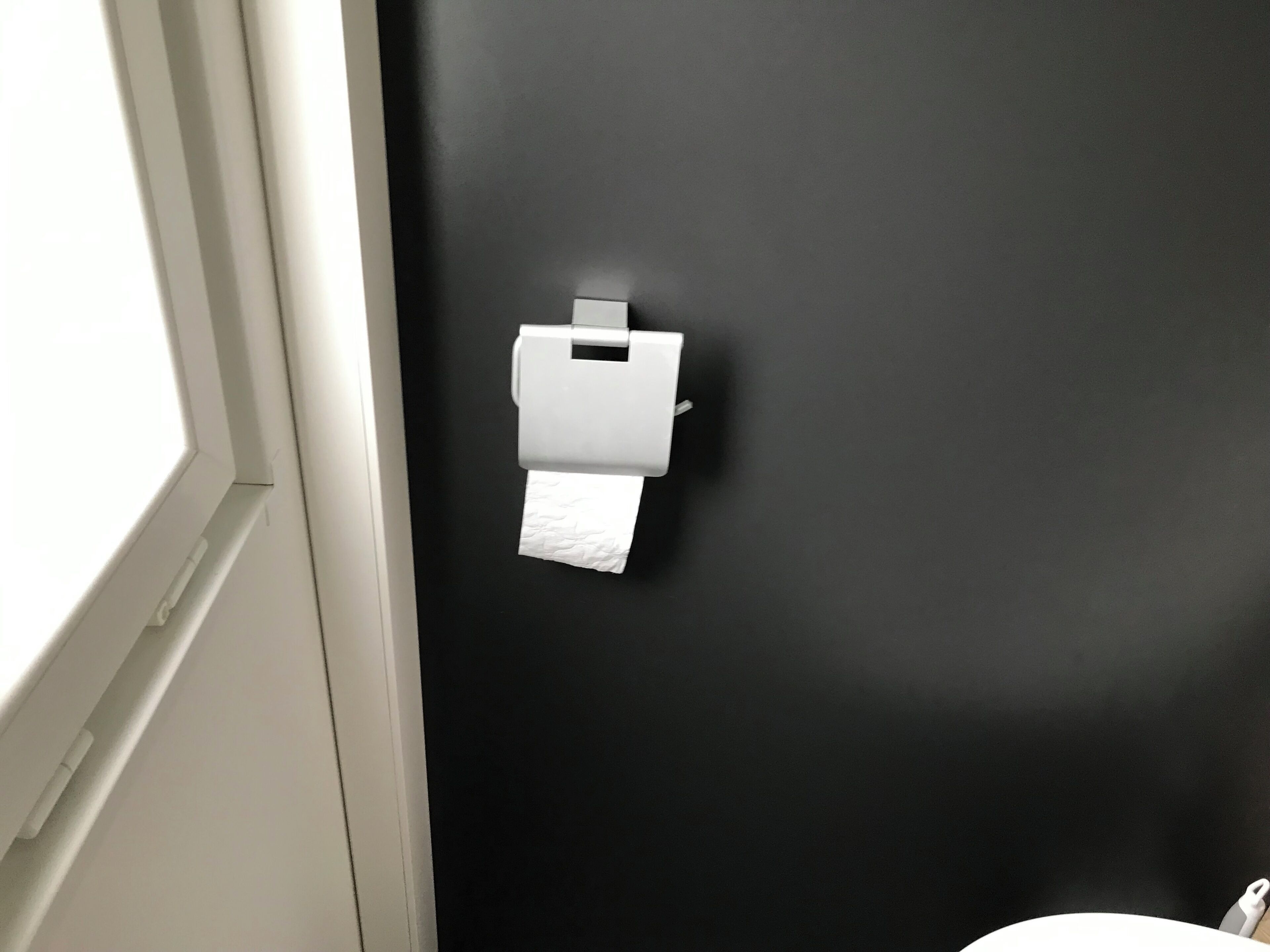 Een zwarte muur met een witte papieren handdoekdispenser.
