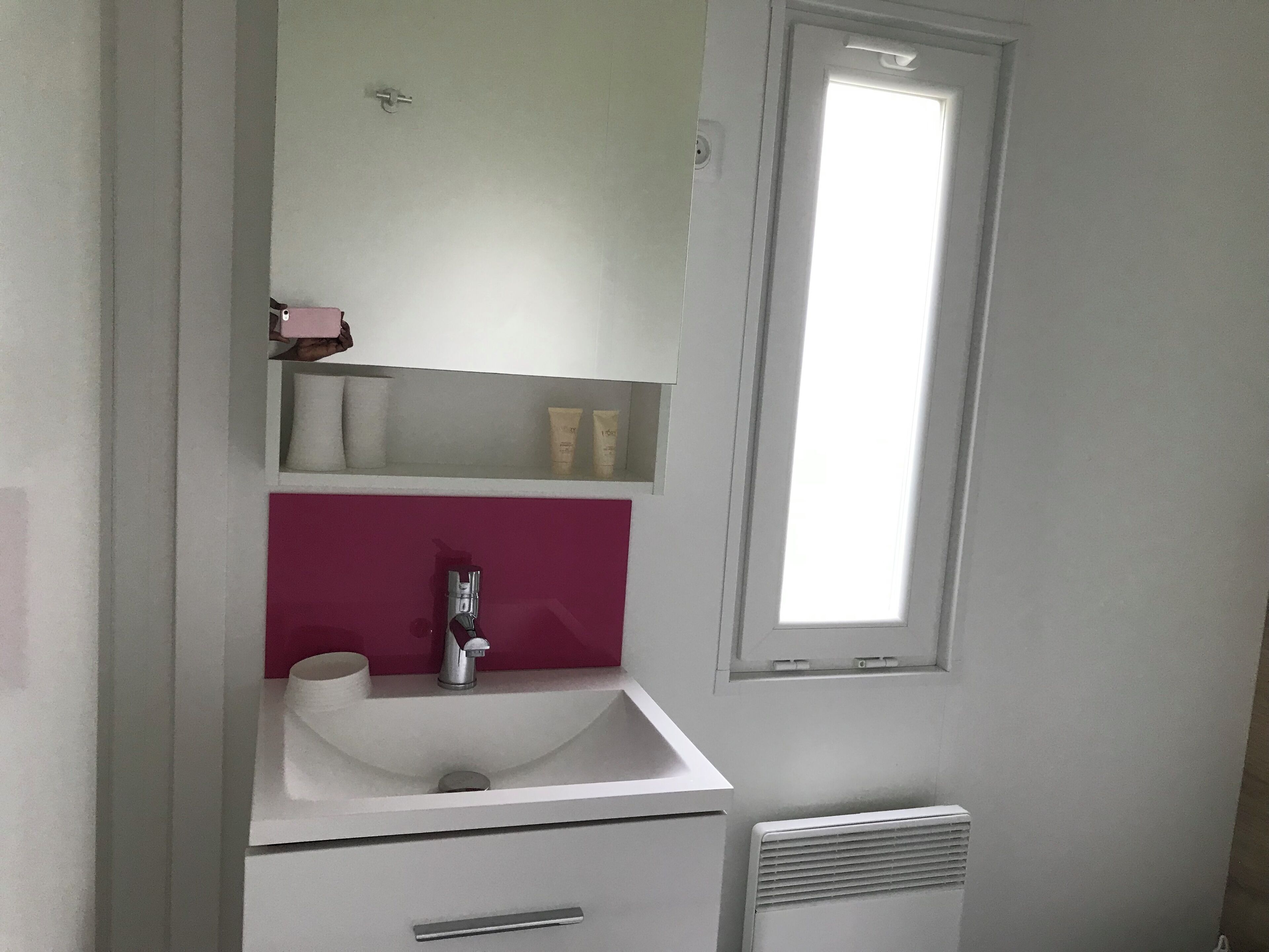 A bathroom with a white sink, a pink vanity, a mirror, and a window.