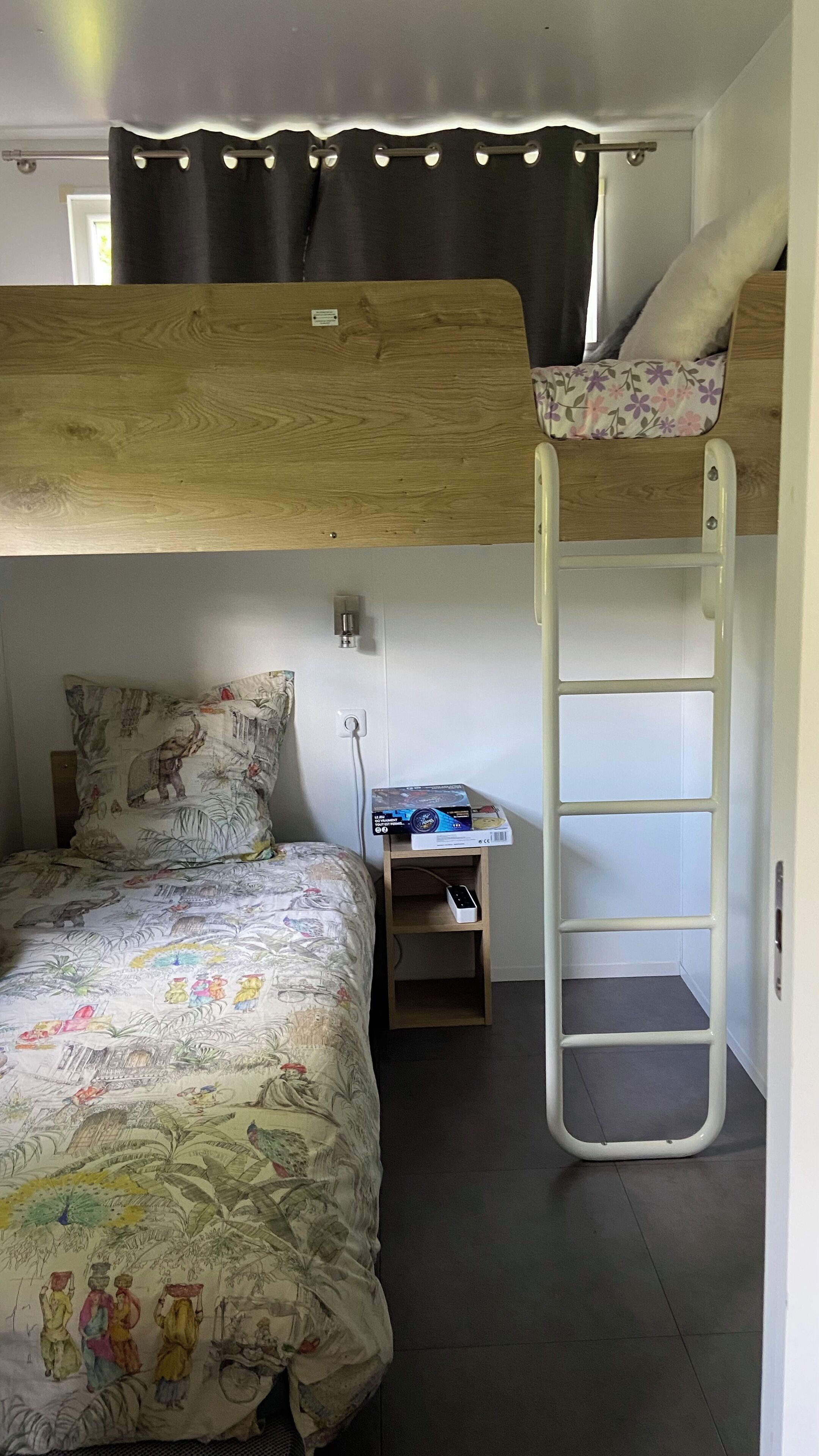 Een slaapkamer met een stapelbed, een houten hoofdbord, een ladder, een bureau met een computer en een bed met een decoratieve spreideken.