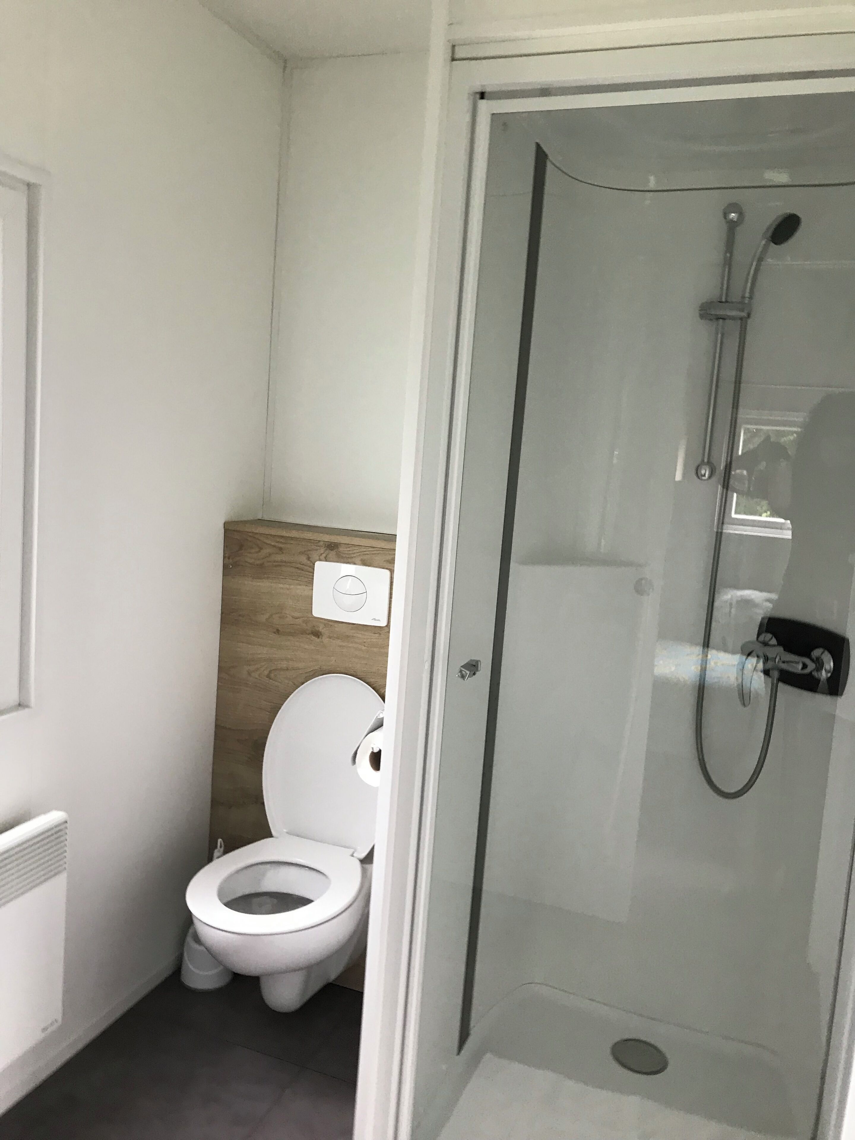 Ein modernes Badezimmer mit Toilette, einer Wand aus Holzpaneelen und einer Duschkabine aus Glas.