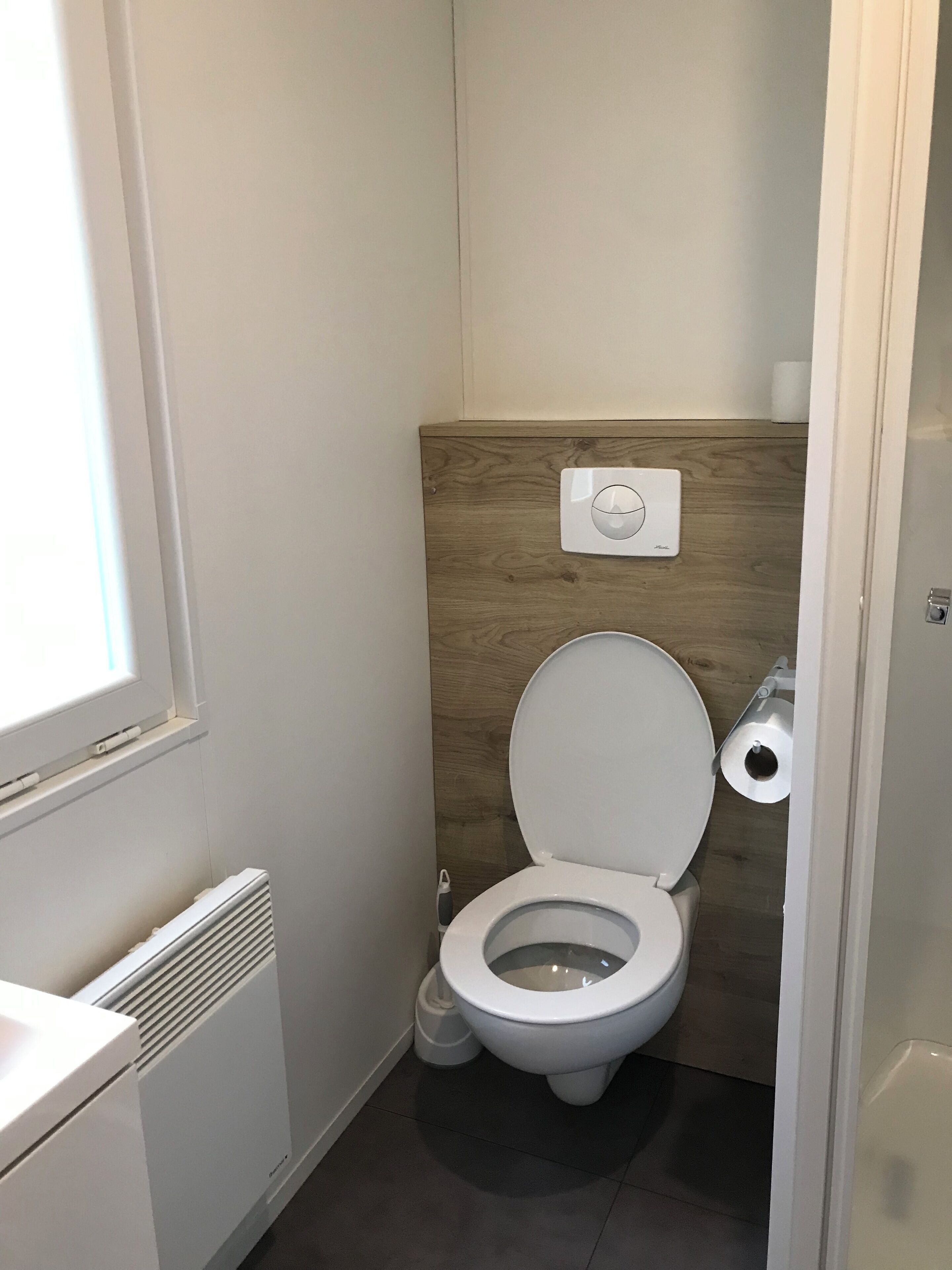 A small, modern bathroom with a toilet, a bidet, and a toilet paper holder on the wall.