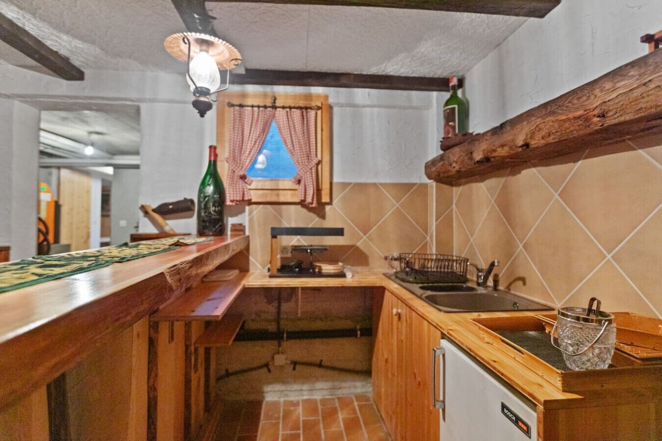Une cuisine compacte avec des plans de travail en bois, un réfrigérateur Bosch, un luminaire suspendu et une fenêtre offrant une belle vue.