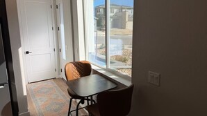 A room with a dining table and chairs, a door, and a large window with a view of the outside. - New Cozy Fully Furnished Studio Lone Tree (Lone Tree)
