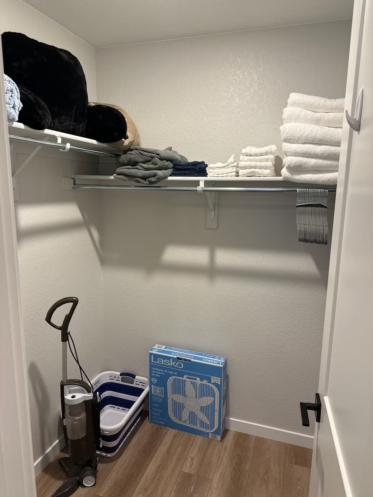 Ein kleiner Abstellraum mit Regalen für Handtücher und einem Luftreiniger von Lasko.
