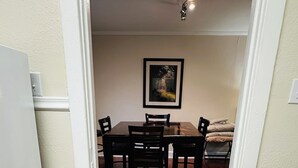 Zona pranzo con tavolo e sedie, un quadro appeso al muro e una lampada a sospensione.