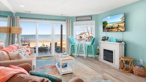 Ein Wohnzimmer mit Blick zum Strand, einem Kamin und einer Essecke mit Stühlen.
