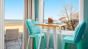 Ein Zimmer mit Blick auf den Strand, ein Tisch mit einem Laptop und zwei Stühle mit türkisfarbenen Kissen.