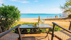 Ein Tisch mit einer Flasche und einem Krug auf einer Terrasse mit Blick auf einen Strand.