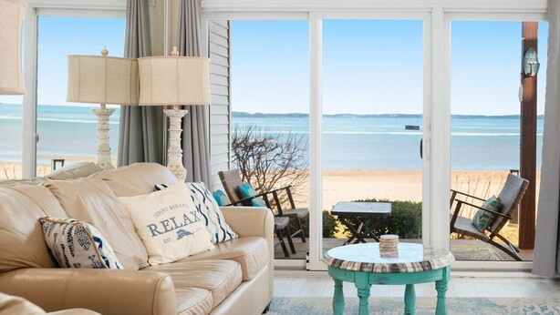 Un salon avec un canapé beige, une table basse de couleur turquoise et une vue sur la plage, visible à travers de grandes portes vitrées.