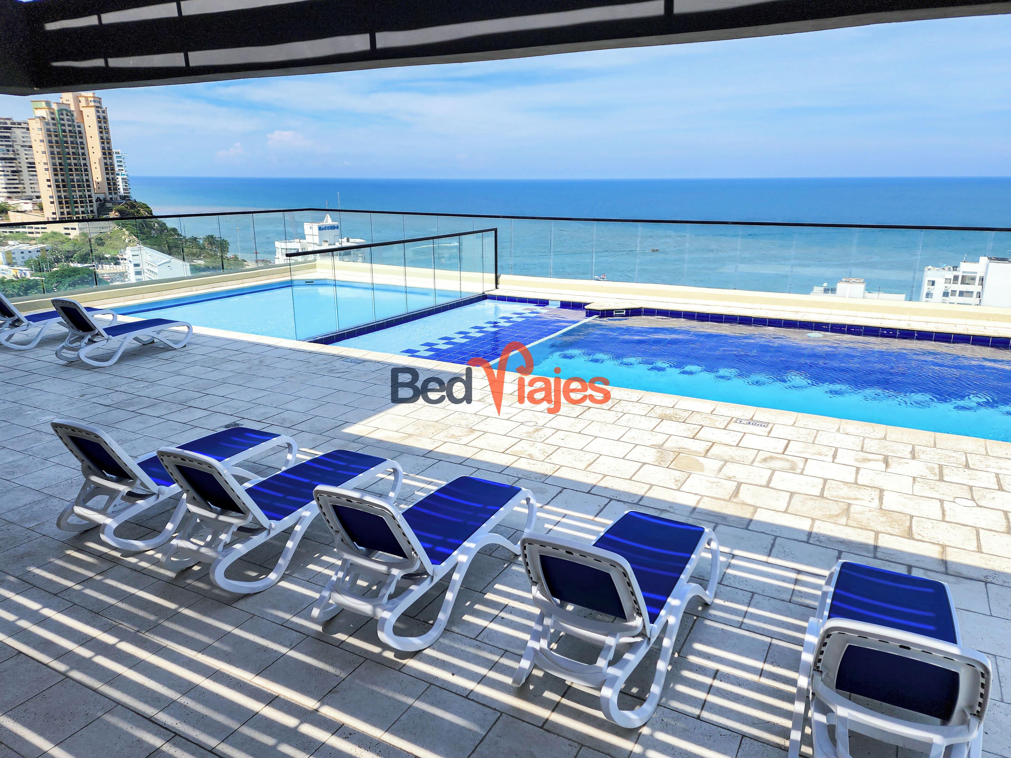 Una piscina en la azotea con sillones reclinables azules y vistas al océano.