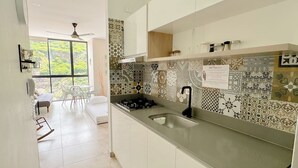 Een moderne keuken met een gasfornuis, een spoelbak en backsplash tegels met een patroon. Door een groot raam is een eethoek met een tafel en stoelen te zien.