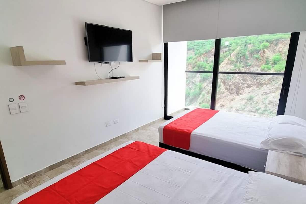 Une chambre d’hôtel avec deux lits, un téléviseur fixé au mur et une grande fenêtre donnant sur un paysage verdoyant.