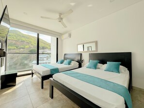 A modern bedroom with two beds, a ceiling fan, a large window with a city view, and a balcony. - Apartasuites Vita 945 - By Bedviajes (Santa Marta)