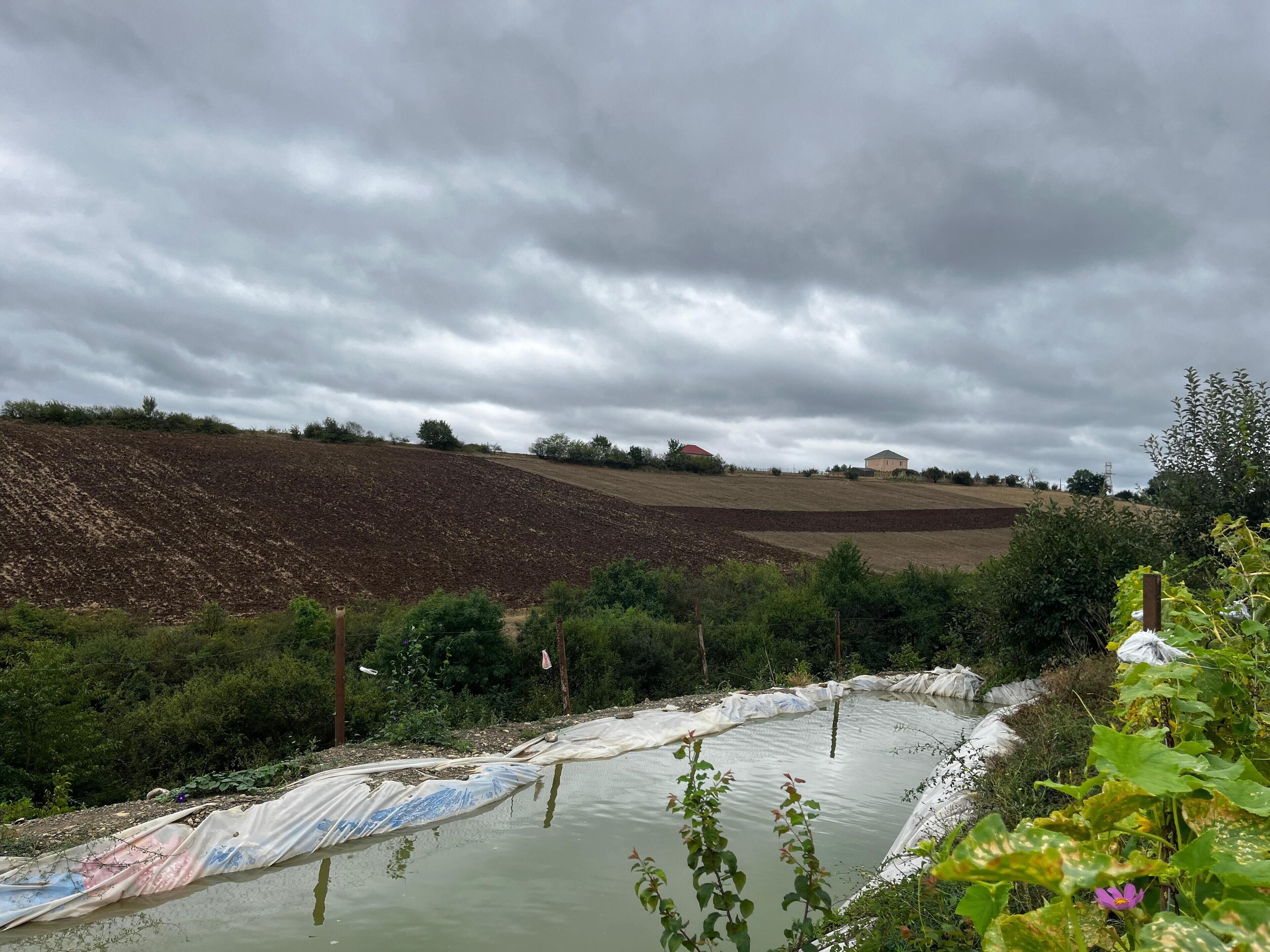 Paisaje rural con un cuerpo de agua, una colina con campos cultivados y un edificio a lo lejos.