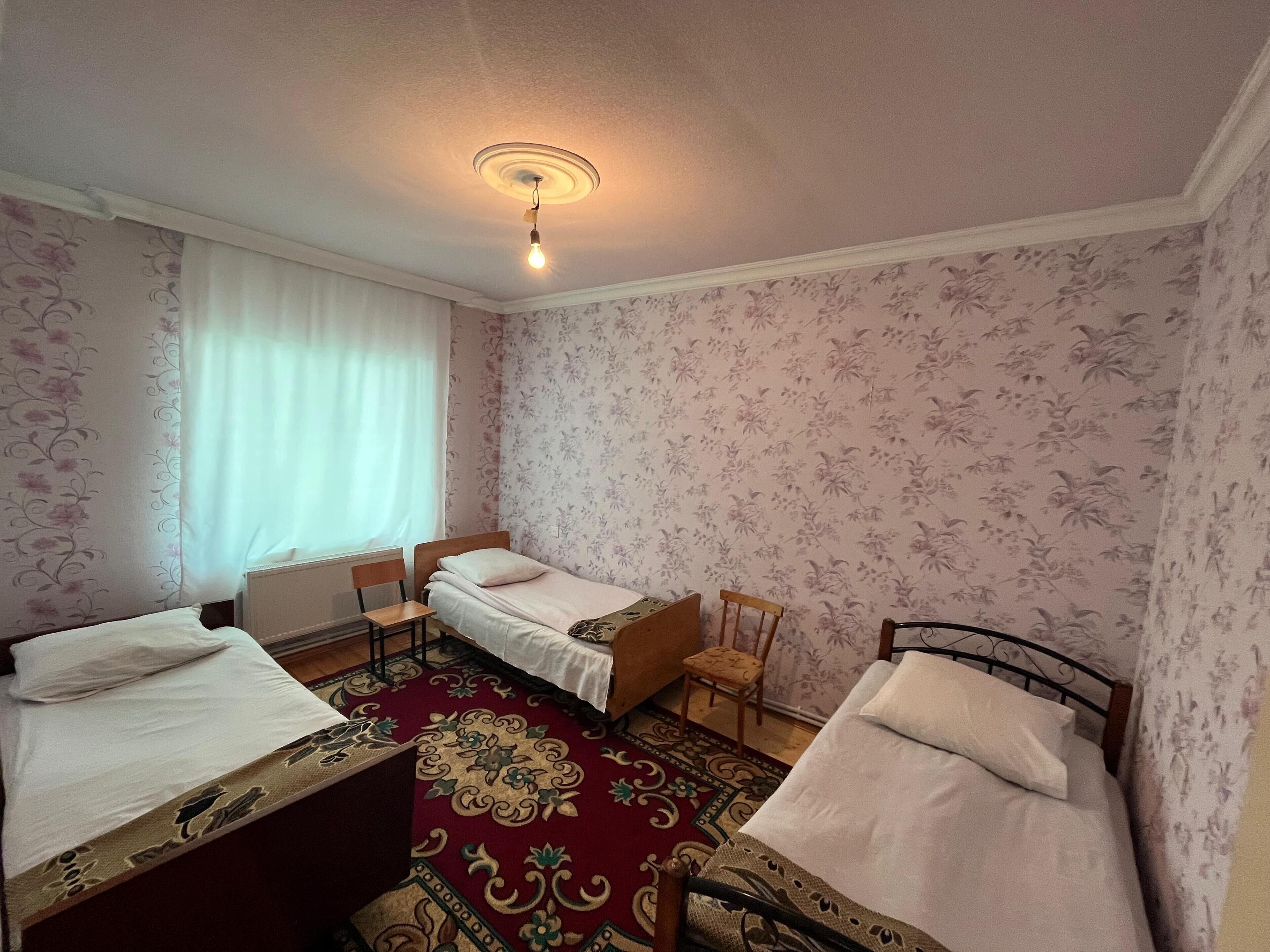 A room with two single beds, a small table, a chair, and a patterned carpet.