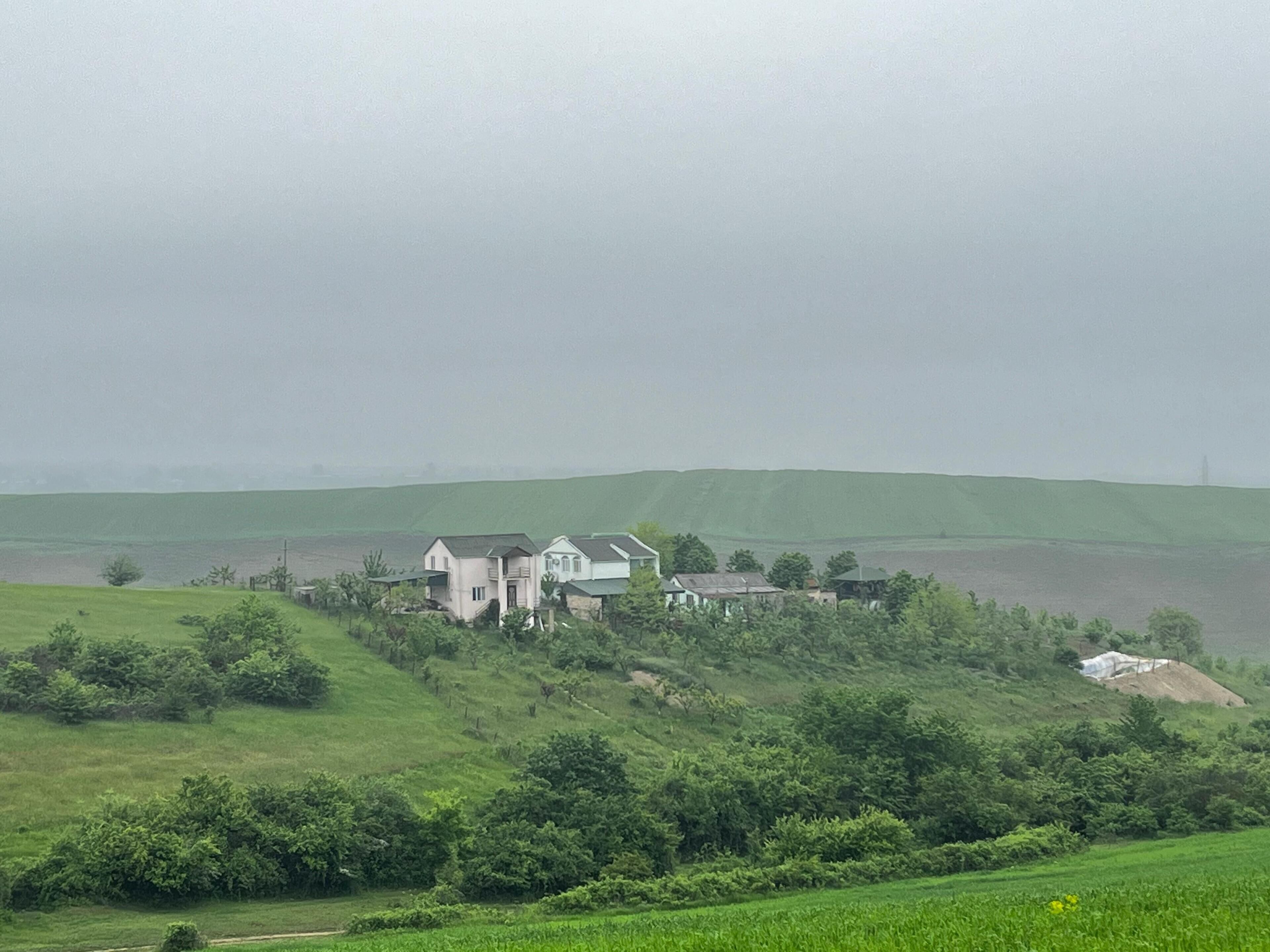 A rural landscape with a large house surrounded by fields and hills.