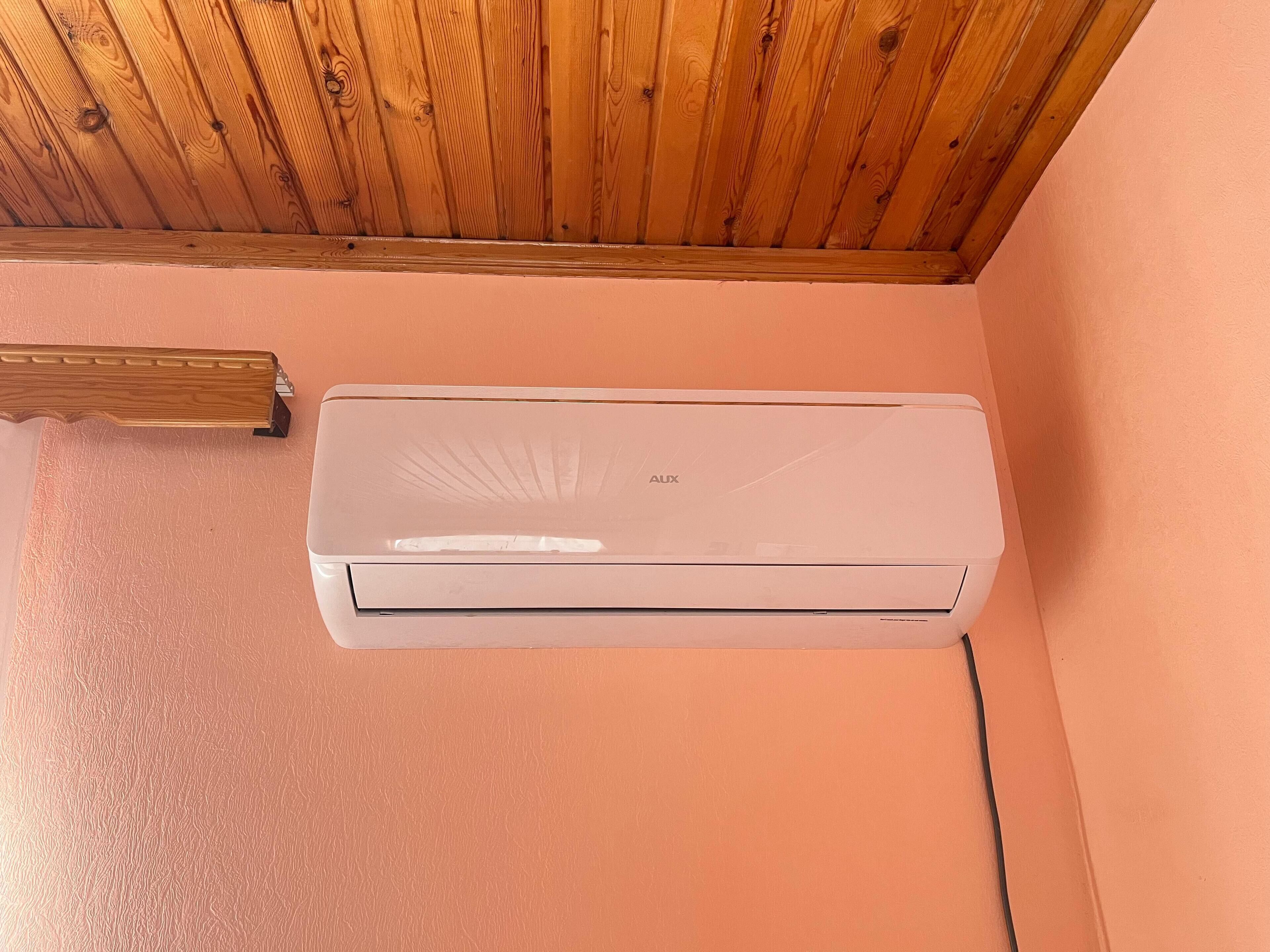 A white air conditioning unit mounted on a peach-colored wall with a wooden ceiling above.