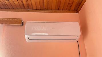 A white air conditioning unit mounted on a peach-colored wall with a wooden ceiling above.