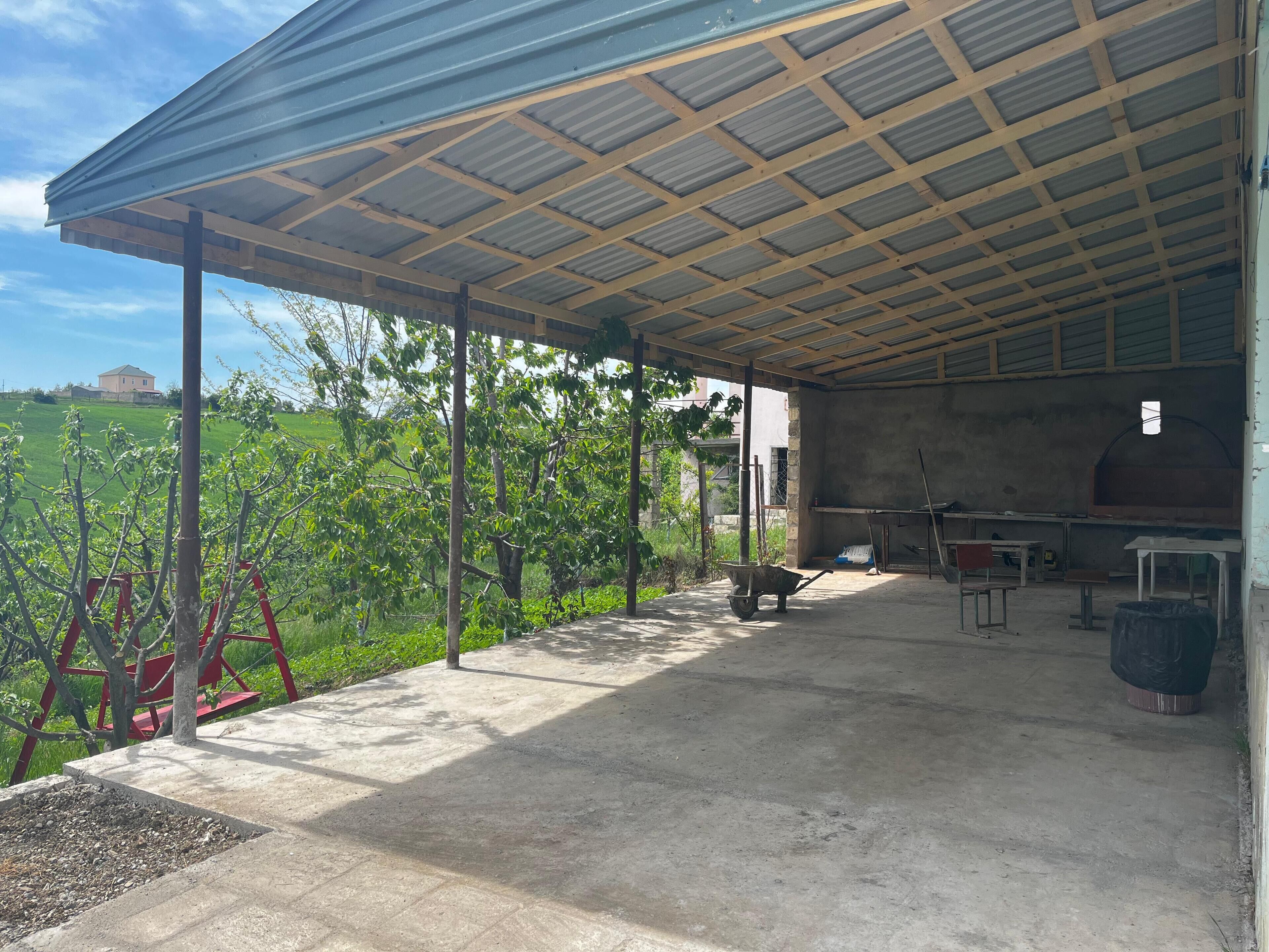 A covered outdoor area with a concrete floor, a wheelbarrow, and a table.