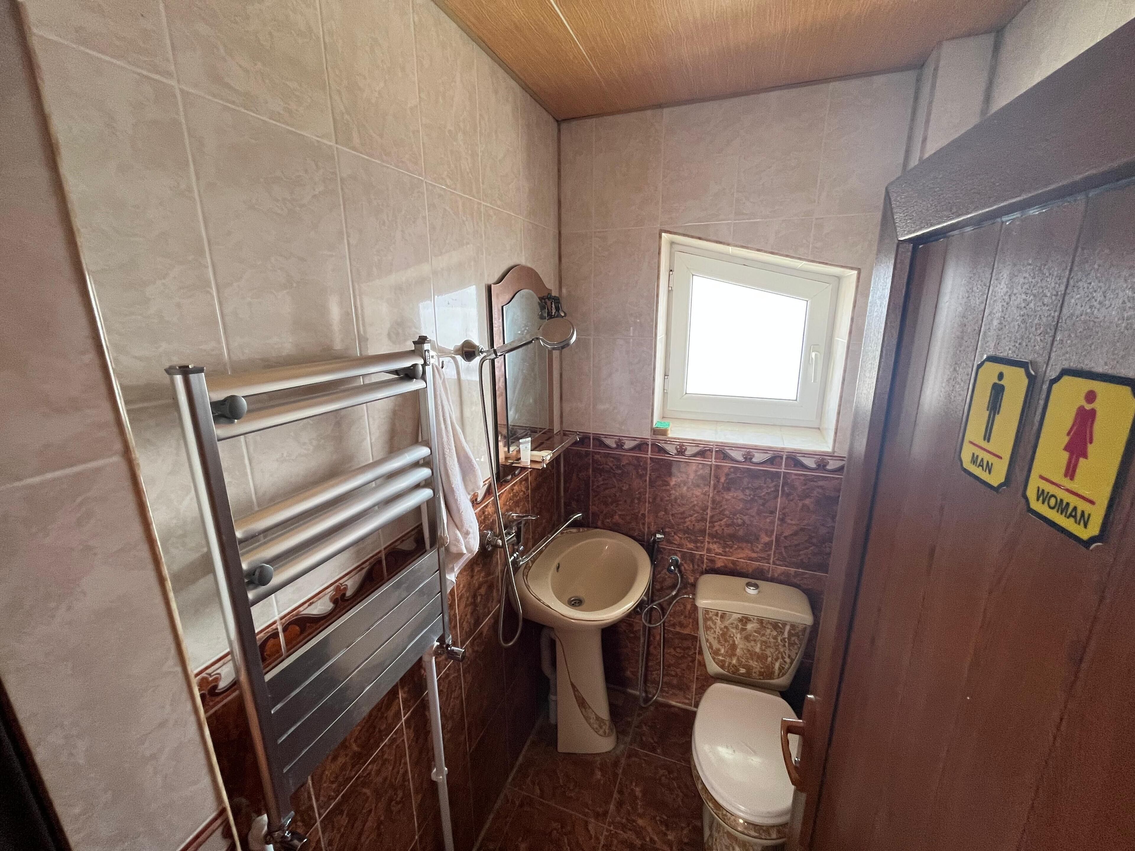 A bathroom with a sink, toilet, and towel rack. There are signs indicating men's and women's facilities.