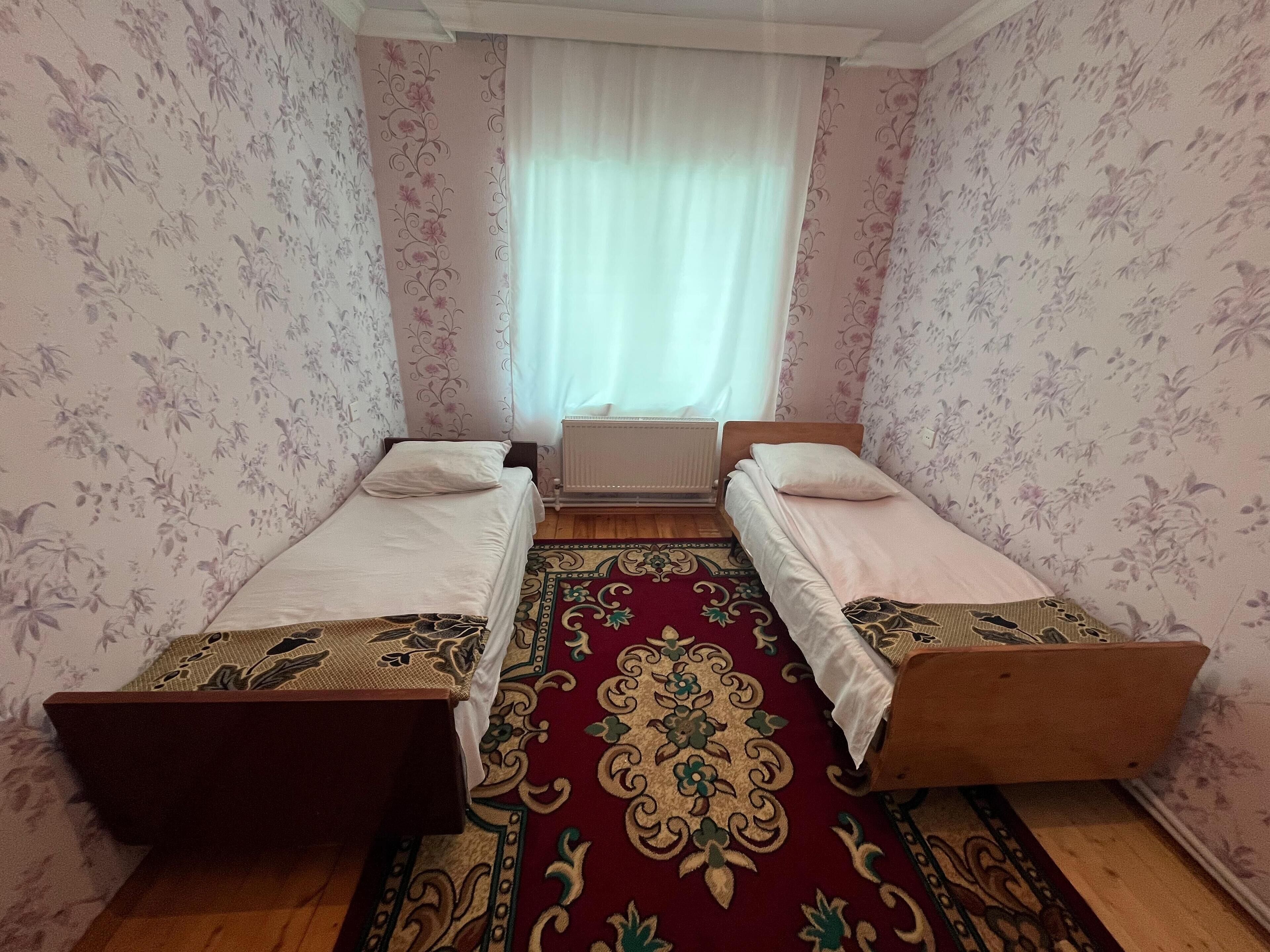 A small, neatly arranged room with two single beds, a radiator, and a patterned carpet.