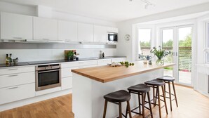 A modern kitchen with white cabinets, a wooden island with bar stools, a built-in oven, and a microwave. - Ref. 673271 (Täby)