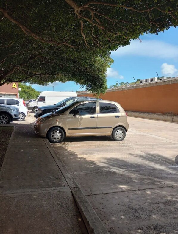 A parking lot with a beige car parked under a tree.