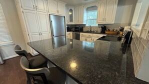 A kitchen with white cabinets, a stainless steel refrigerator, a granite countertop, and a bar stool. - Lazy Days on Neely Henry with kayaks and floating mat! (Ashville)
