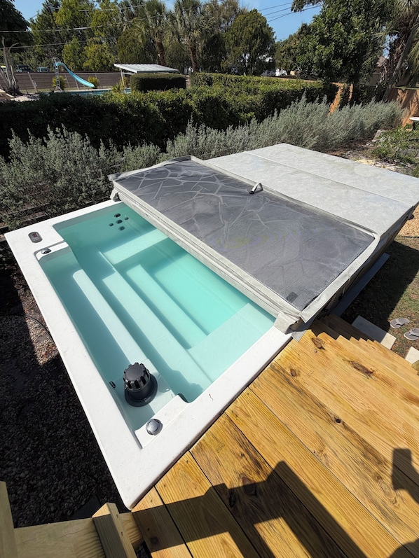 A hot tub with a mesh cover, surrounded by a wooden deck and a pool.