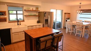 Una cocina moderna con una isla central, armarios blancos y una zona de comedor con sillas y mesa blancos.
