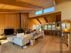 A modern interior with a large sofa, a TV, a fireplace, a kitchen area, and a bar. - True North | Bluff Top Trails | The Sea Ranch (Sea Ranch)