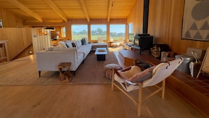Ein geräumiges Wohnzimmer mit einem großen Sofa, einem Kamin und Blick ins Freie.