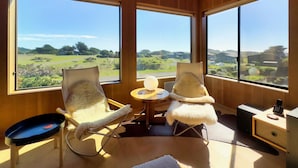 Ein Zimmer mit zwei Stühlen, einem kleinen Tisch und Blick auf eine grüne Landschaft durch große Fenster.