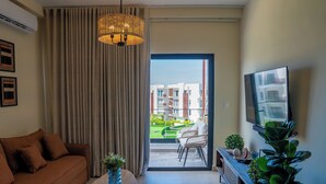 Una sala de estar moderna con un sofá, una mesa de centro con un florero, un televisor en la pared y un balcón con vistas a edificios.