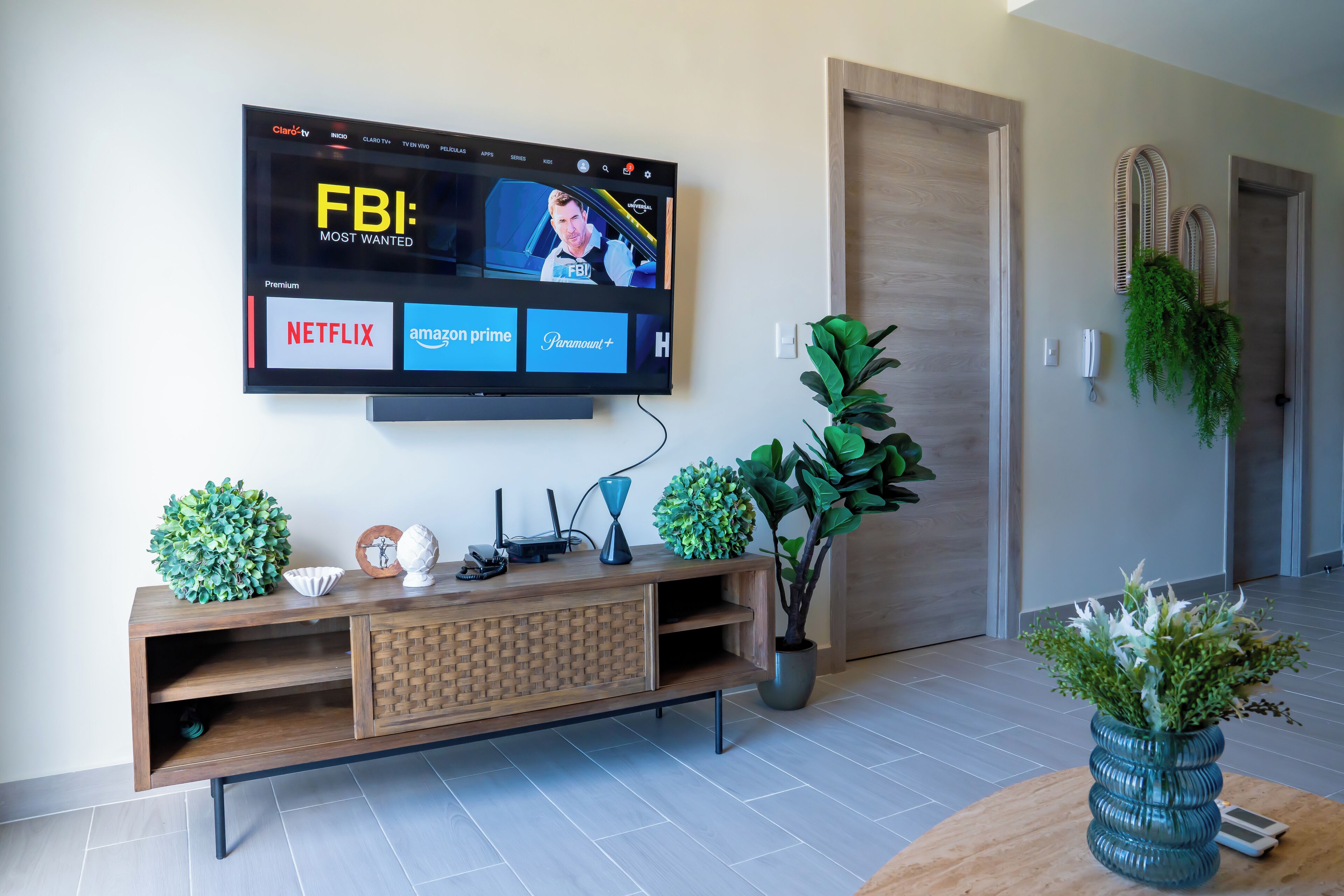 Un salón moderno con un televisor de pantalla plana montado en la pared mostrando la interfaz de un servicio de streaming.