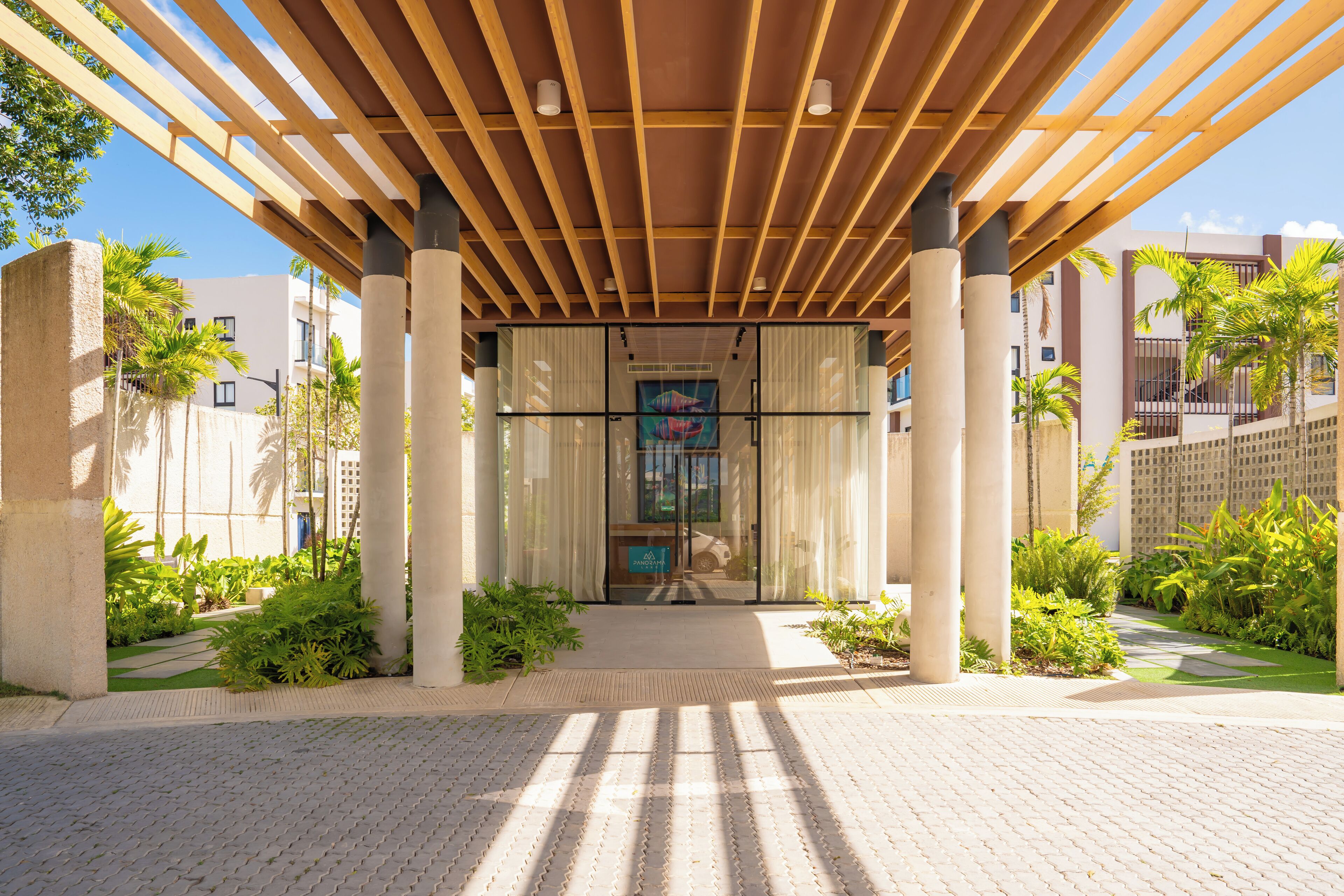 A covered entrance with a wooden pergola, glass doors, and a pathway leading to a building.