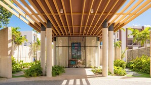 Una entrada cubierta con una pérgola de madera, puertas de cristal y un camino que lleva a un edificio.
