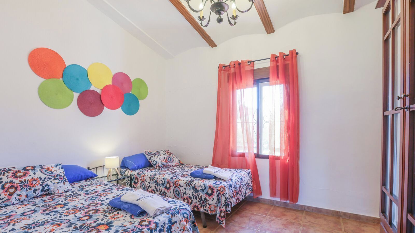 Une chambre avec deux lits, une fenêtre ornée de rideaux rouges et un mur décoré de motifs circulaires colorés.