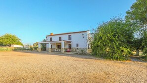 A two-story white building with a stone foundation, a covered patio with outdoor seating, and a gravel driveway. - Casa Rural El Pantano Peñarroya-Pueblonuevo by Ruralidays (Córdoba)