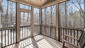 A covered porch with large windows, a ceiling fan, and a view of a wooded area.