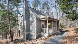 A small cabin with a porch, surrounded by trees.