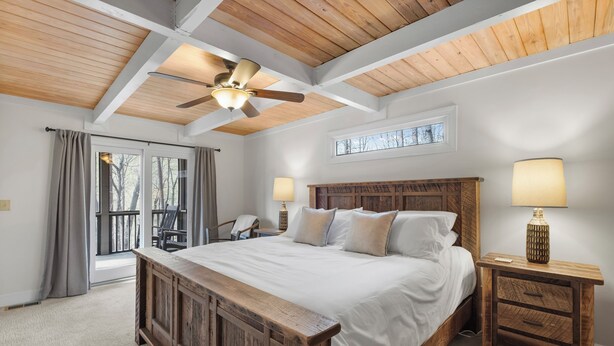 A bedroom with a wooden bed, a ceiling fan, a nightstand with a lamp, and a window with curtains.