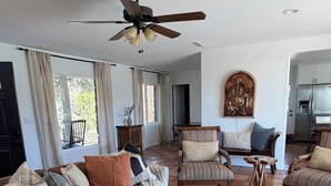 Ein großzügiges Wohnzimmer mit braunem Ledersofa, gestreiften Sesseln, einem runden Couchtisch und einem Deckenventilator.